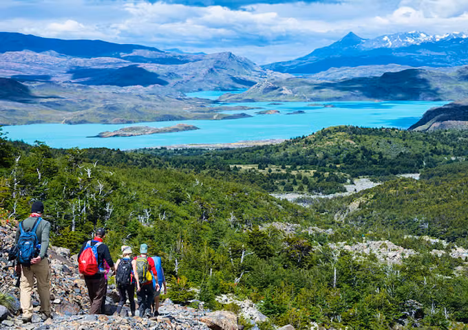 Group of hikers in the French Valley, above a forest, a turquoise blue lake and a mountain backdrop, Torres del Paine Hike, Chile