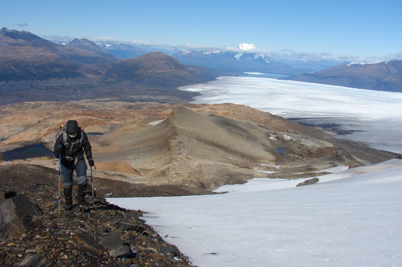 One hiker with poles climbing up Zapata Mountain with snow and glaciers behind in Torres del Paine National Park. Torres del Paine Hike, Chile