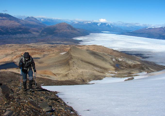 One hiker with poles climbing up Zapata Mountain with snow and glaciers behind in Torres del Paine National Park. Torres del Paine Hike, Chile
