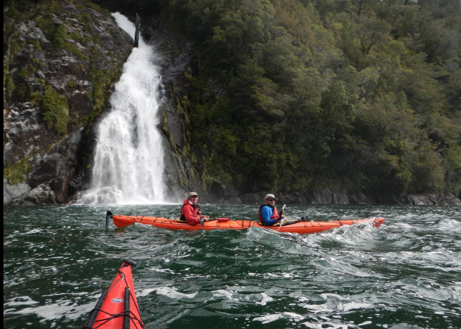 Kayaking by waterfalls during a multi-day kayak in Pumalín Park, Patagonia, Chile