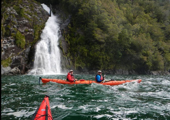 Kayaking by waterfalls during a multi-day kayak in Pumalín Park, Patagonia, Chile