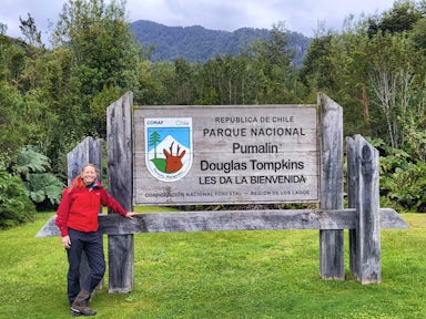 A hiker stands at the sign showing the entrance to Pumalín Doug;as Tompkins National Park in Chile
