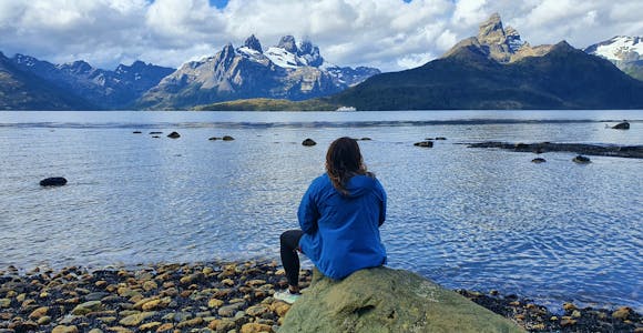 Tourist sitting on the beach looking across the water to snowy mountains in Tierra del Fuego