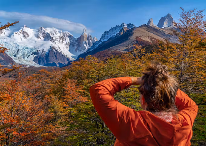 A hiker looks out over the autumn colours of trees to the snowcapped Fitzroy mountain range in Los Glaciares national park Argentina