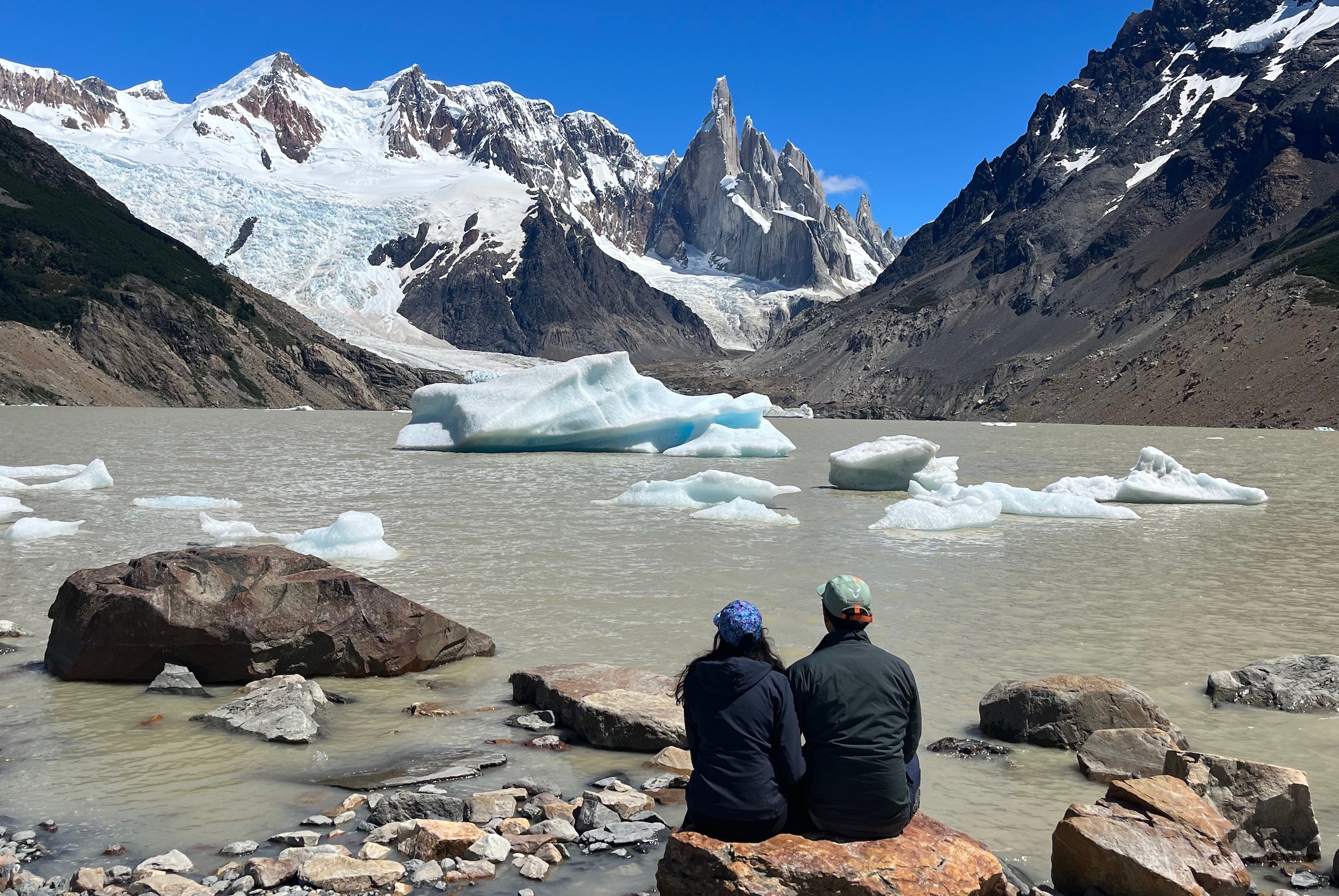 Two hikers sit by Laguna Torre looking at Cerro Torre on a day hike from El Chaltén