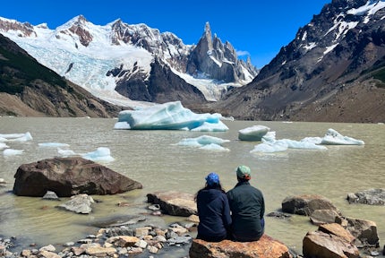 Two hikers sit by Laguna Torre looking at Cerro Torre on a day hike from El Chaltén