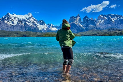 Tourist with feet in lake facing the Cuernos of Torres del Paine