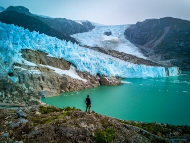 A hiker standing looking at the snout of the Lenoes glacier in Aysen Chile as it calves into the water