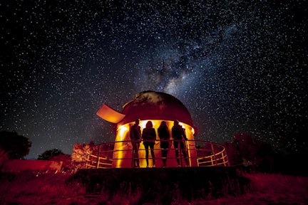 A group of people stand silhouetted outside a telescope observatory near San Pedro in Chile's Atacama Desert. The night sky is full of stars, with the Milky Way clearly visible.